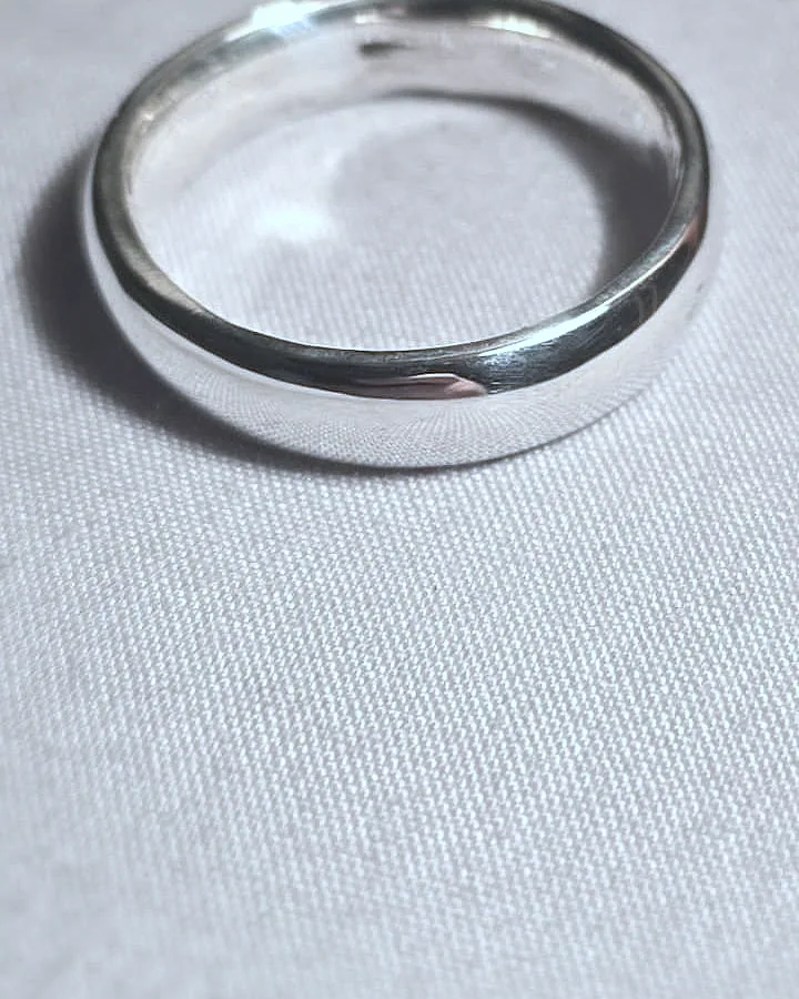 A thin silver band standing on plain cream cloth. (finished product)