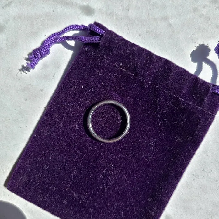 A thin silver band centred on a purple velvet pouch. (finished product)