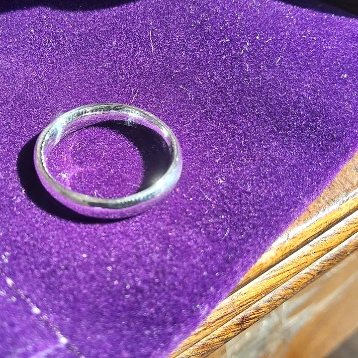 A thin polished silver band on a purple velvet pouch. (finished product)
